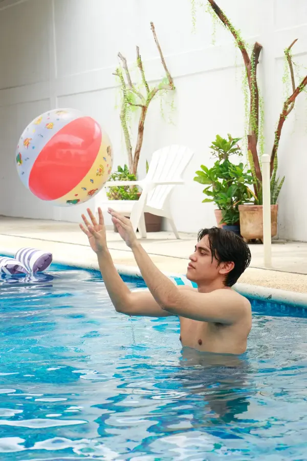 Joven jugando con una pelota de playa dentro de la alberca